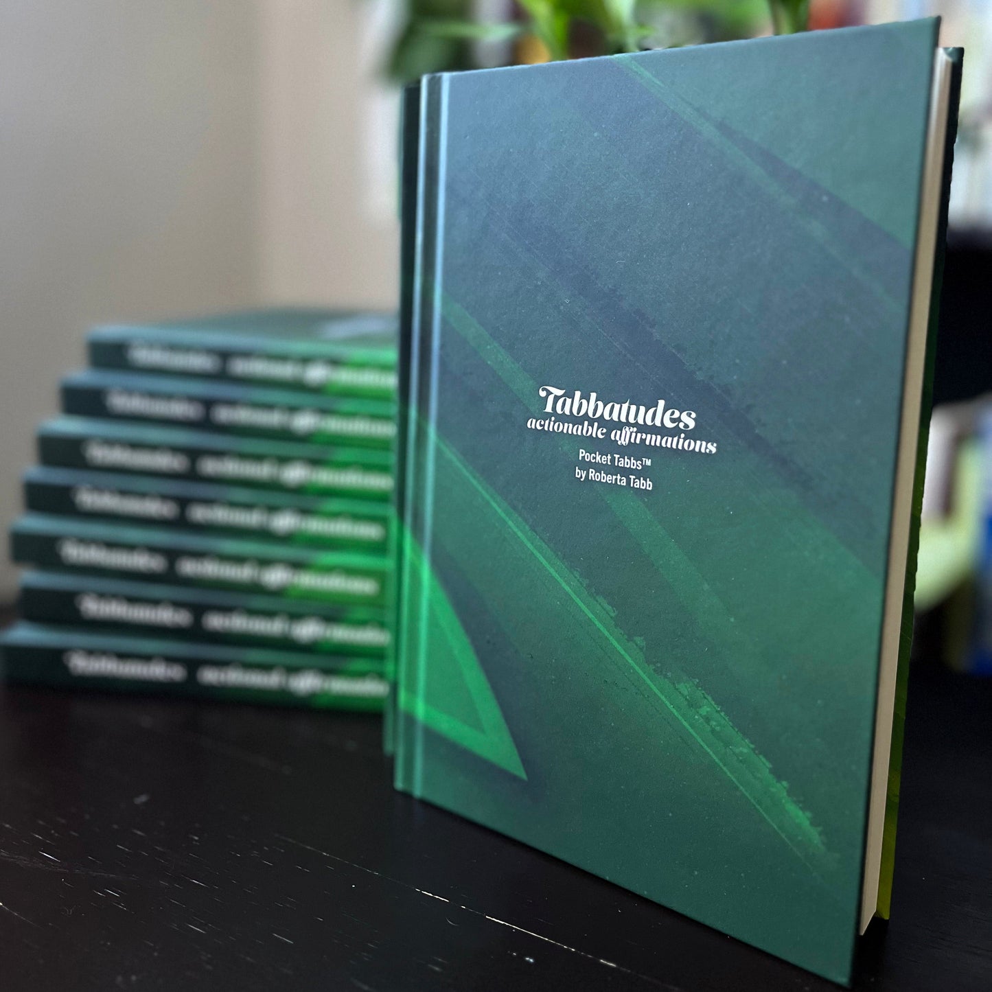 A book titled 'TABBATUDES: Actionable Affirmations' by Roberta Tabb, displayed on a table with a blurred background.