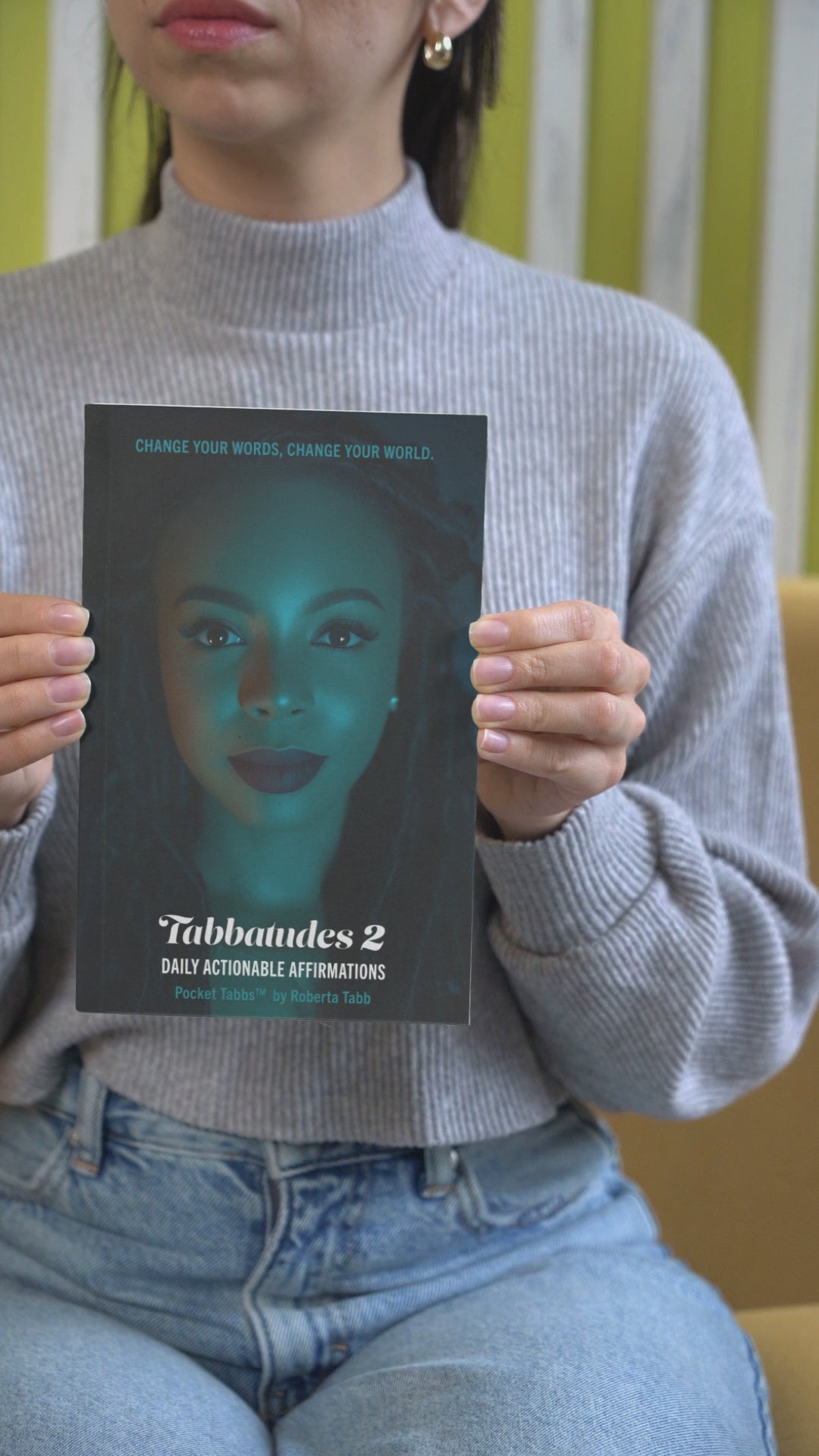 Woman holding Tabbatudes 2 Daily Actionable Affirmations book by Roberta Tabb